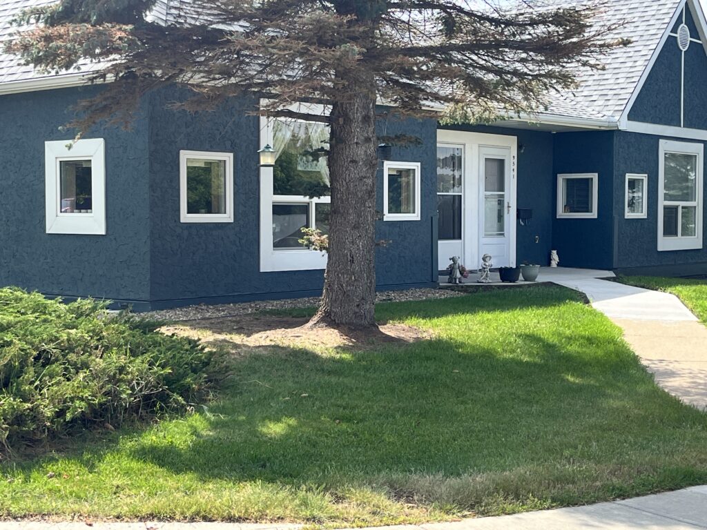 Single-storey residential units with pitched roofs and mature trees along the sidewalk