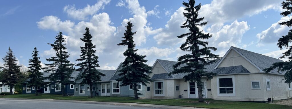 Single-storey residential units with pitched roofs and mature trees along the sidewalk