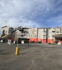 Apartment building under repair with fencing, construction equipment, and protective barriers in front of the structure