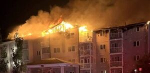 Apartment building with active fire along the roof and visible flames at night